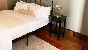 A bedroom with a bed, a bedside table with a lamp, and a wooden floor. - Amazing experience near the Quinnipiac River. Historic w/chef's kitchen & bidet. (New Haven)