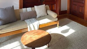 A living room with a sofa, a round wooden coffee table, and a pendant light. There are two wooden doors and framed pictures on the wall. - Amazing experience near the Quinnipiac River. Historic w/chef's kitchen & bidet. (New Haven)