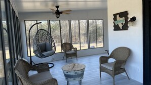 A sunlit room with wicker furniture, a ceiling fan, and large windows offering a view of the outdoors.