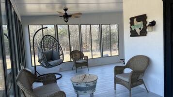 A sunlit room with wicker furniture, a ceiling fan, and large windows offering a view of the outdoors.