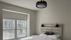 A bedroom with a bed, a window with blinds, and a ceiling light fixture.