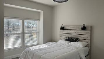 A bedroom with a bed, a window with blinds, and a ceiling light fixture.