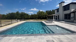 A rectangular swimming pool with a tiled deck, surrounded by a black metal fence.
