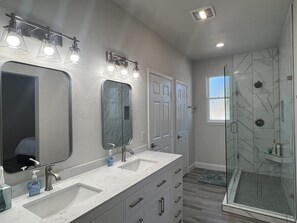 A modern bathroom with a large mirror, two sinks, a shower with glass doors, and a vanity with drawers. - Experience Elegance at our Luxury Ranch with New Pool & Deck (Celina)