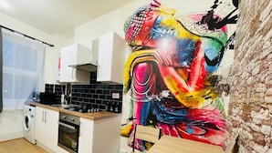 Uma cozinha moderna com armários brancos, forno embutido e fogão preto. Um quadro abstrato e colorido decora a parede.