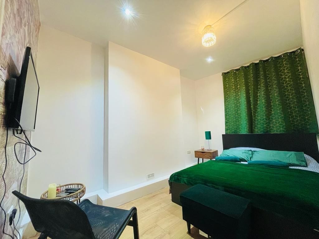 A bedroom with a bed, a chair, a bedside table, and a television mounted on the wall.