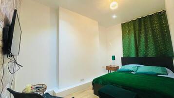 A bedroom with a bed, a chair, a bedside table, and a television mounted on the wall.