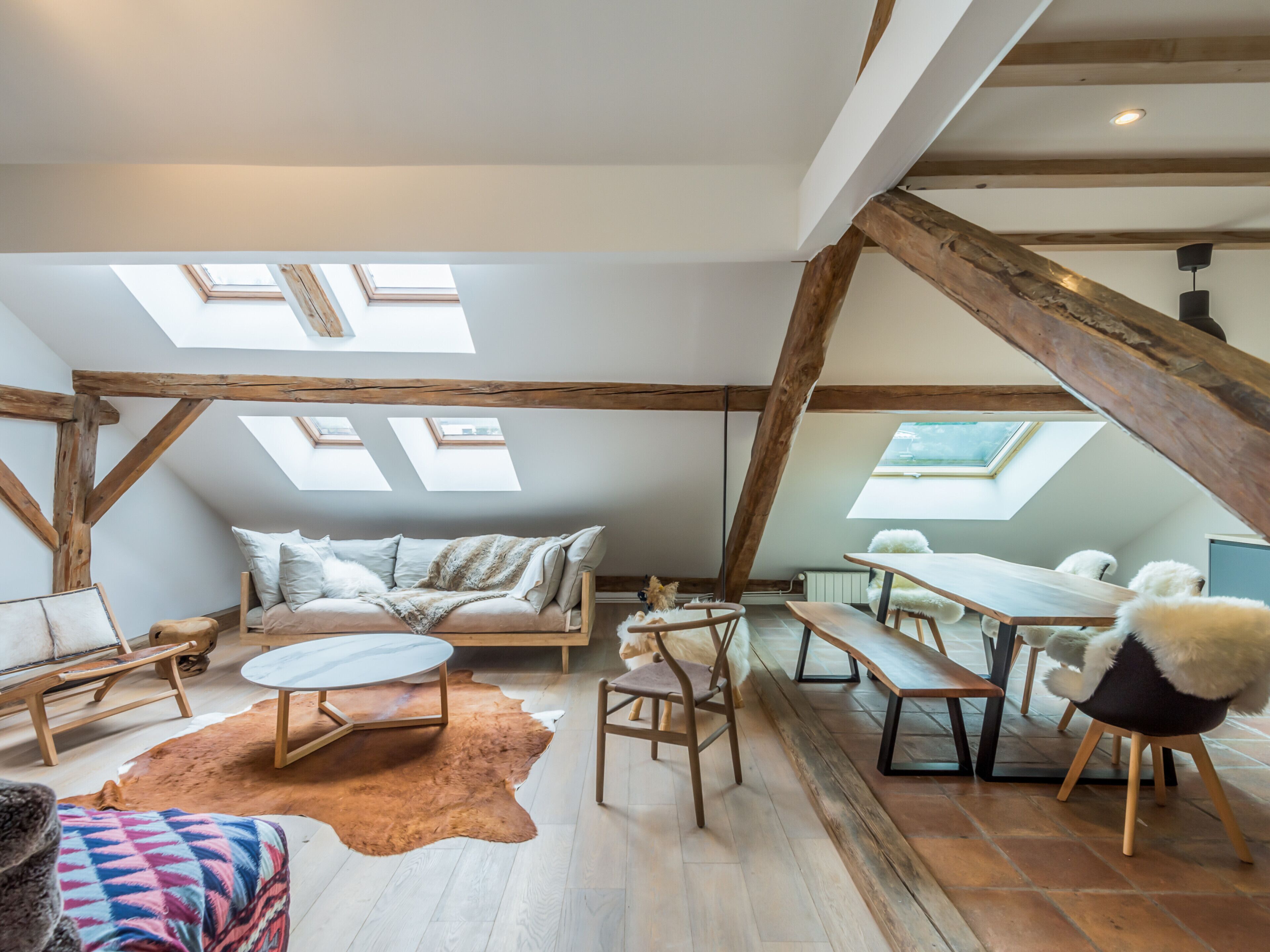 A loft-style room with exposed wooden beams, a sofa, a dining table, and a small dog.