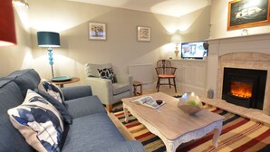 Una sala de estar acogedora con chimenea, sofá, mesa de centro y televisor.