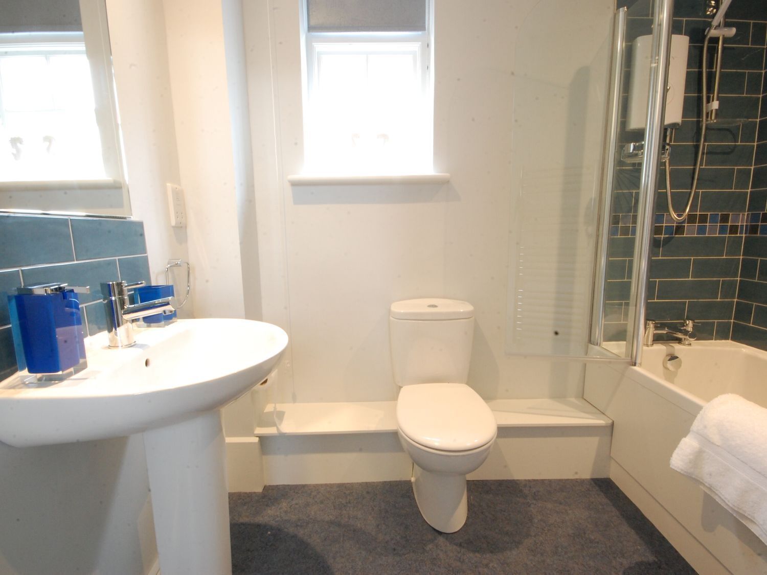 Une salle de bain avec un lavabo, des toilettes et une baignoire, tous de couleur blanche. Il y a également un espace douche doté d’une porte en verre.