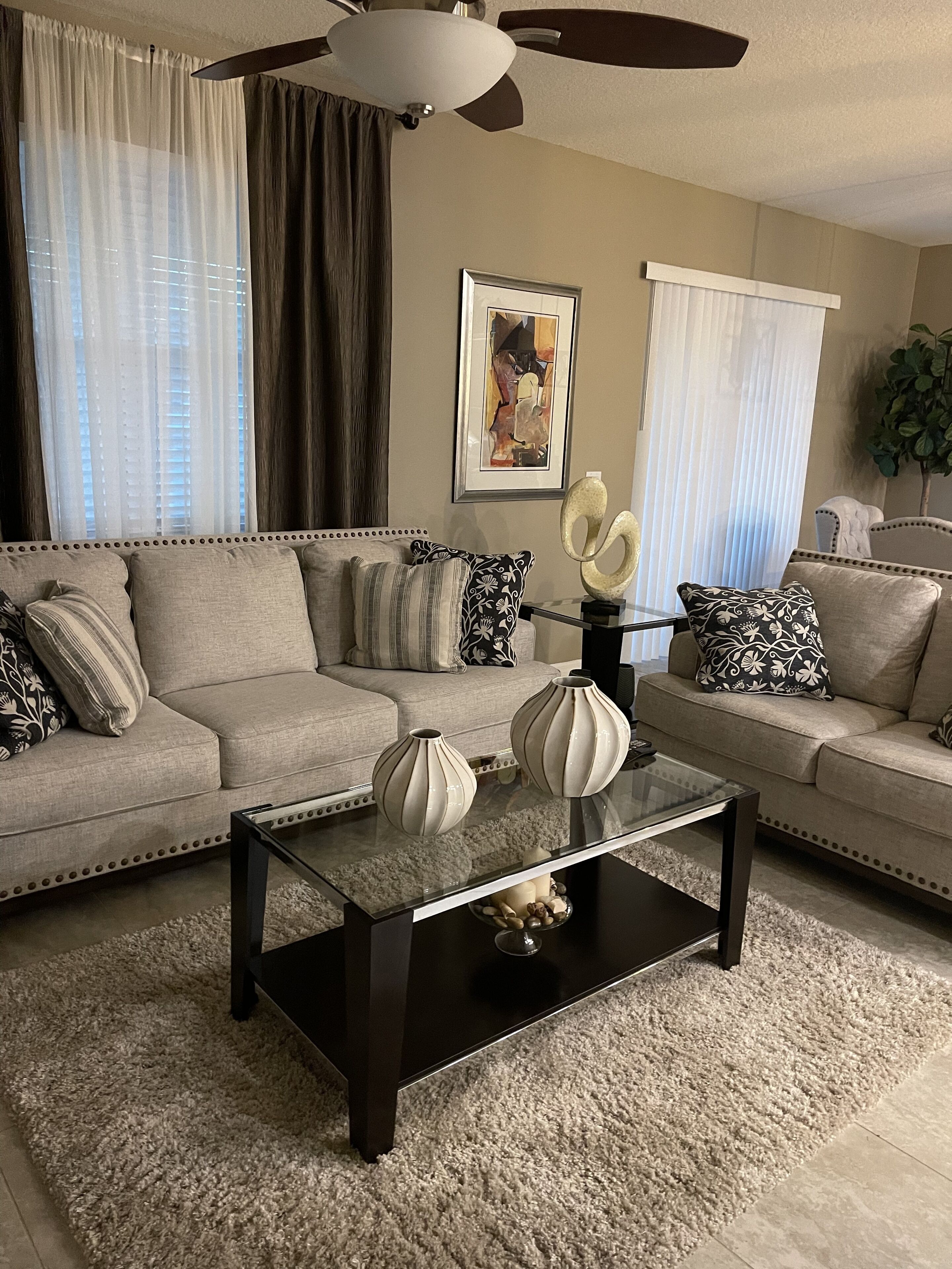 A living room with a beige sofa, a dark coffee table with decorative vases, and a ceiling fan.