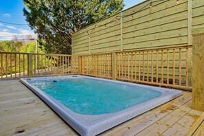 Un bain à remous sur une terrasse en bois, avec une clôture en bois et des arbres en arrière-plan.