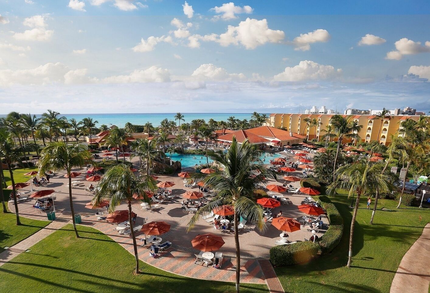 A resort with a central pool, palm trees, and a view of the ocean.