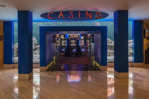 Entrada a un casino con un letrero llamativo, una zona de bar y máquinas tragamonedas.
