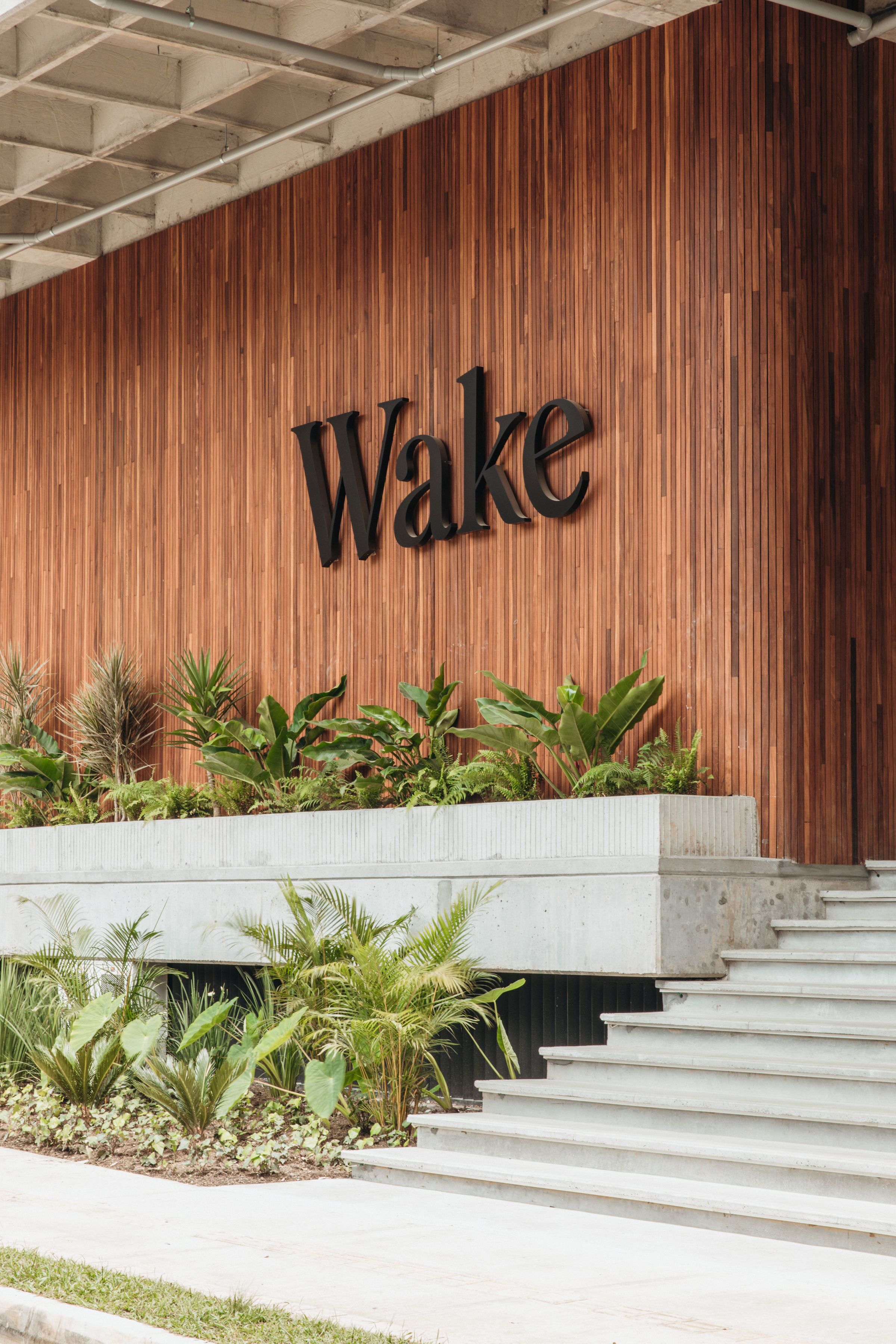 Un mur en bois sur lequel est inscrit le mot « Wake » en grandes lettres, un escalier en béton et un bac à fleurs contenant diverses plantes.