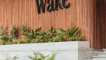 Un mur en bois sur lequel est inscrit le mot « Wake » en grandes lettres, un escalier en béton et un bac à fleurs contenant diverses plantes.