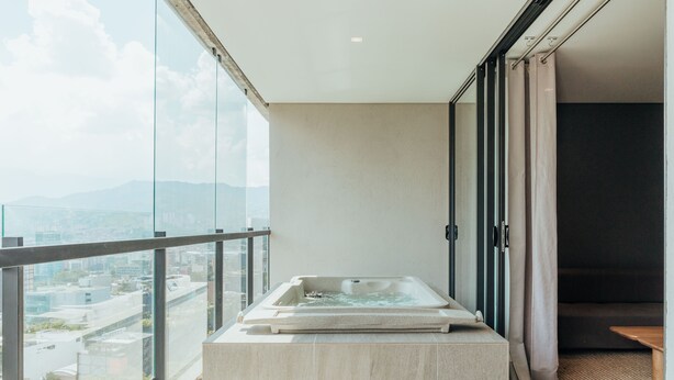 Un baño moderno con una bañera de hidromasaje acristalada en un balcón, con vistas a la ciudad.