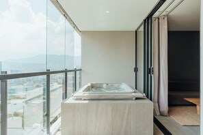 A modern bathroom with a glass-enclosed jacuzzi on a balcony, offering a city view.