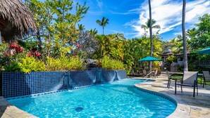 A swimming pool with a tiled edge, surrounded by lush greenery and palm trees. - Oceanview Townhome, freshly updated in Keauhou, close to Kona. (Keauhou)