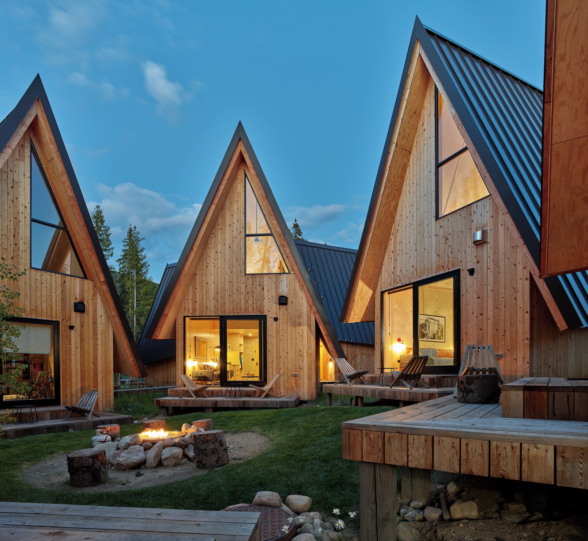 A modern wooden cabin with triangular architecture, large windows, and outdoor seating.