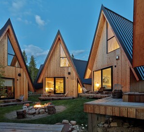 Une cabane moderne en bois, dotée d’une architecture triangulaire, de grandes fenêtres et d’un espace salon extérieur.