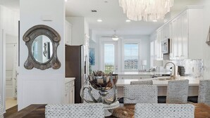 A modern kitchen with white cabinetry, a chandelier, and a dining area with a white table and chairs. - SPECTACULAR, LUX, BEACHFRONT Villa/ WOW Views/Steps to Beach & Resort/WIFI/Pool (Galveston)