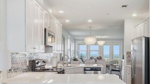 A modern kitchen with white cabinetry, a large island, and a view to the ocean. - SPECTACULAR, LUX, BEACHFRONT Villa/ WOW Views/Steps to Beach & Resort/WIFI/Pool (Galveston)