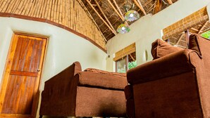 Una habitación con techo de bambú, una puerta de madera y dos sofás marrones.