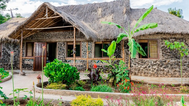 Una casa de piedra tradicional con techo de paja, un porche de madera y un jardín con diversas plantas y flores.