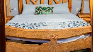 Una cama de madera con un cabecero sencillo, un almohadón de estampado geométrico y una pared lisa.