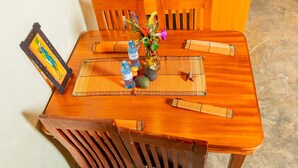 Una mesa de madera para comer con un mantel individual, dos botellas de agua, un jarrón con flores y un cuadro enmarcado.