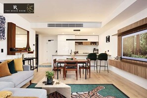 Un salon moderne comprenant un canapé, une table basse et un coin repas avec des chaises et une table. Il y a également une cuisine équipée de placards et une fenêtre donnant sur une forêt.