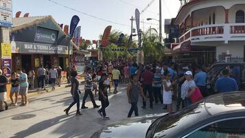 Rua movimentada com pedestres e carros, apresentando um bar esportivo 'MAR & TIERRA SPORT BAR' e um edifício 'MEDALLA'.