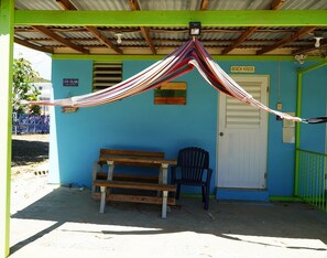 Un espace extérieur abrité, aménagé avec un hamac, un banc et une chaise.