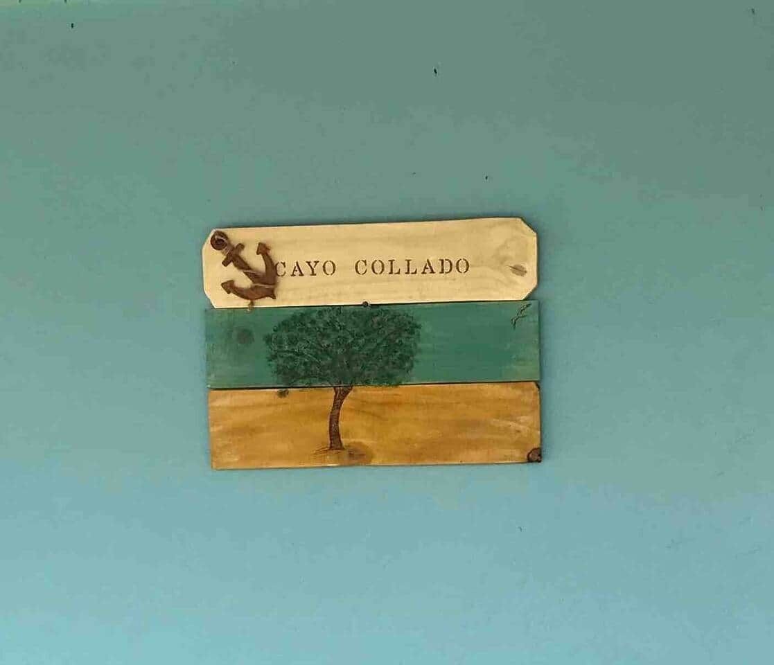 Et flag med et træ og teksten "CAYO COLLADO" mod en turkis baggrund.