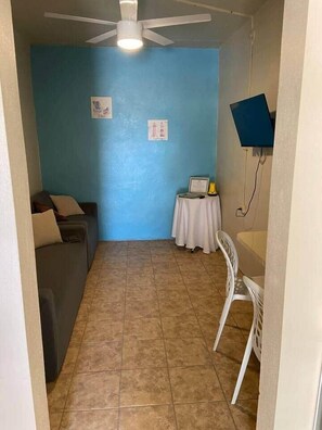 Un pasillo estrecho con ventilador de techo, pared azul, una mesita con una silla y un televisor montado en la pared.