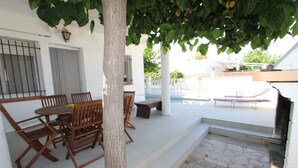Un patio con mesa y sillas, una piscina y una pared blanca con una ventana.