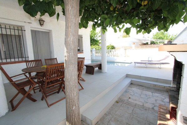 A patio with a table and chairs, a pool, and a white wall with a window.