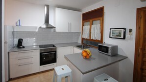 Una cocina moderna con armarios blancos, una campana extractora de acero inoxidable, un microondas y una pequeña isla con un frutero.