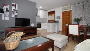 Una sala de estar moderna con un televisor de pantalla plana, una mesa de centro de vidrio y una cesta de mimbre.