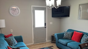 Ein Wohnzimmer mit zwei smaragdgrünen Sofas, einem gemusterten Teppich, einem Fernseher und einer Tür mit Fenster.