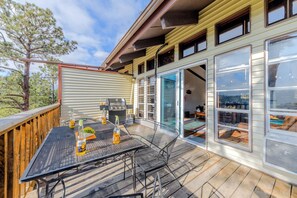 A wooden deck with a metal table and chairs, a grill, and a glass door leading inside.