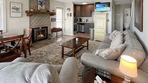 Ein Wohnzimmer mit Kamin, Sofa, Couchtisch und einem über der Küche montierten Fernseher.