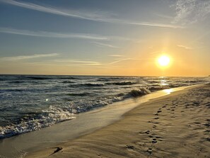 Une plage où l’on voit des empreintes de pas menant à l’eau, des vagues et un coucher de soleil.