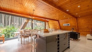 A modern kitchen with a large island, wooden ceiling, and large windows overlooking a forest. - Woodpecker, Weybourne, Norfolk (Weybourne)