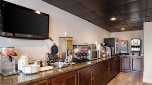 A kitchen area with a coffee machine, microwave, and a large flat-screen TV mounted on the wall. - Super 8 by Wyndham Daleville/Fort Novosel (Daleville)