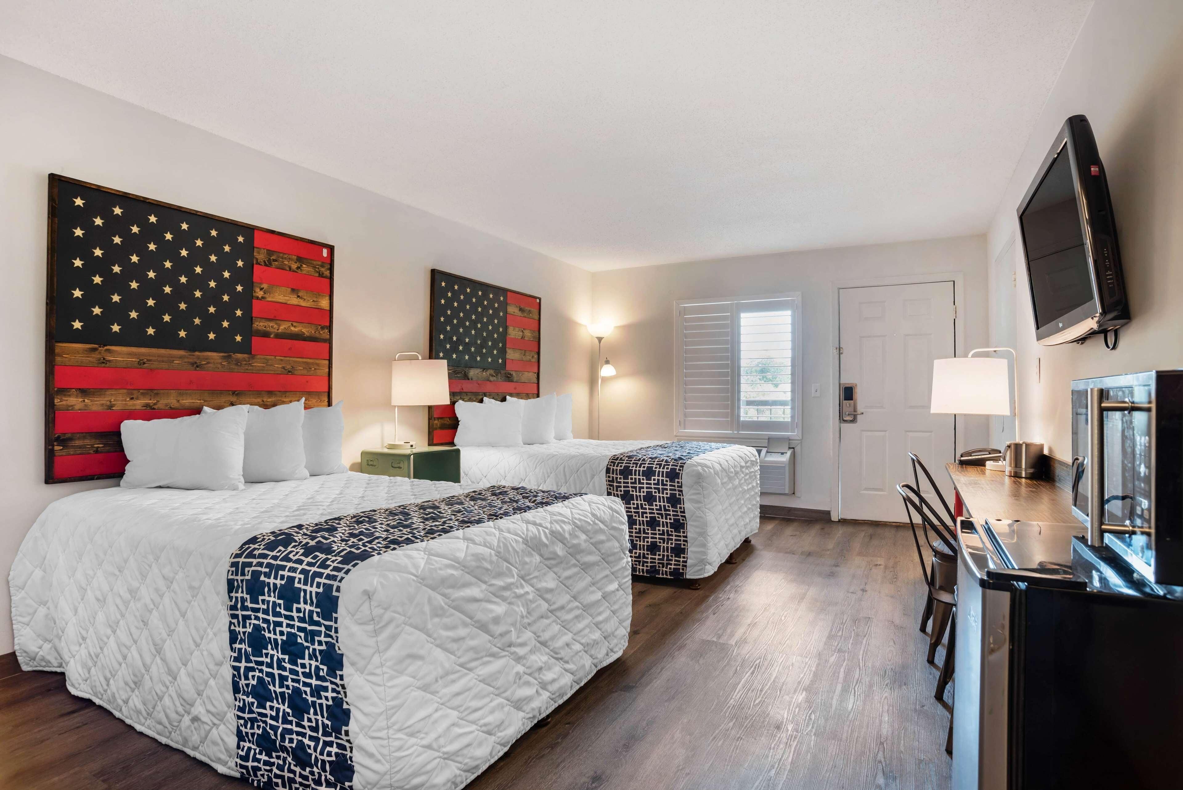 A hotel room with two beds, a TV, a desk, and artwork on the walls.