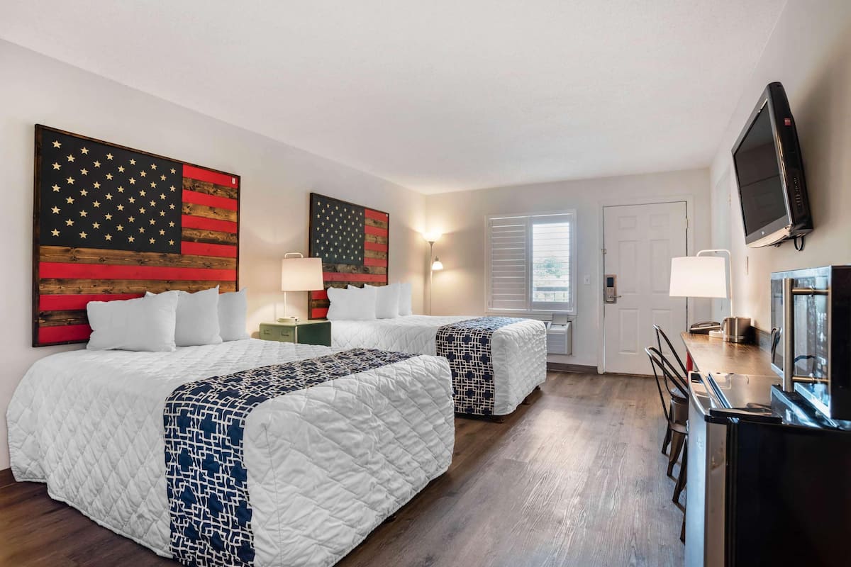 A hotel room with two beds, a TV, a desk, and artwork on the walls.