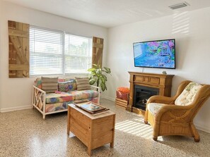 Una sala de estar con sofá, sillón, mesa de centro, chimenea, televisor y un ventanal con persianas.