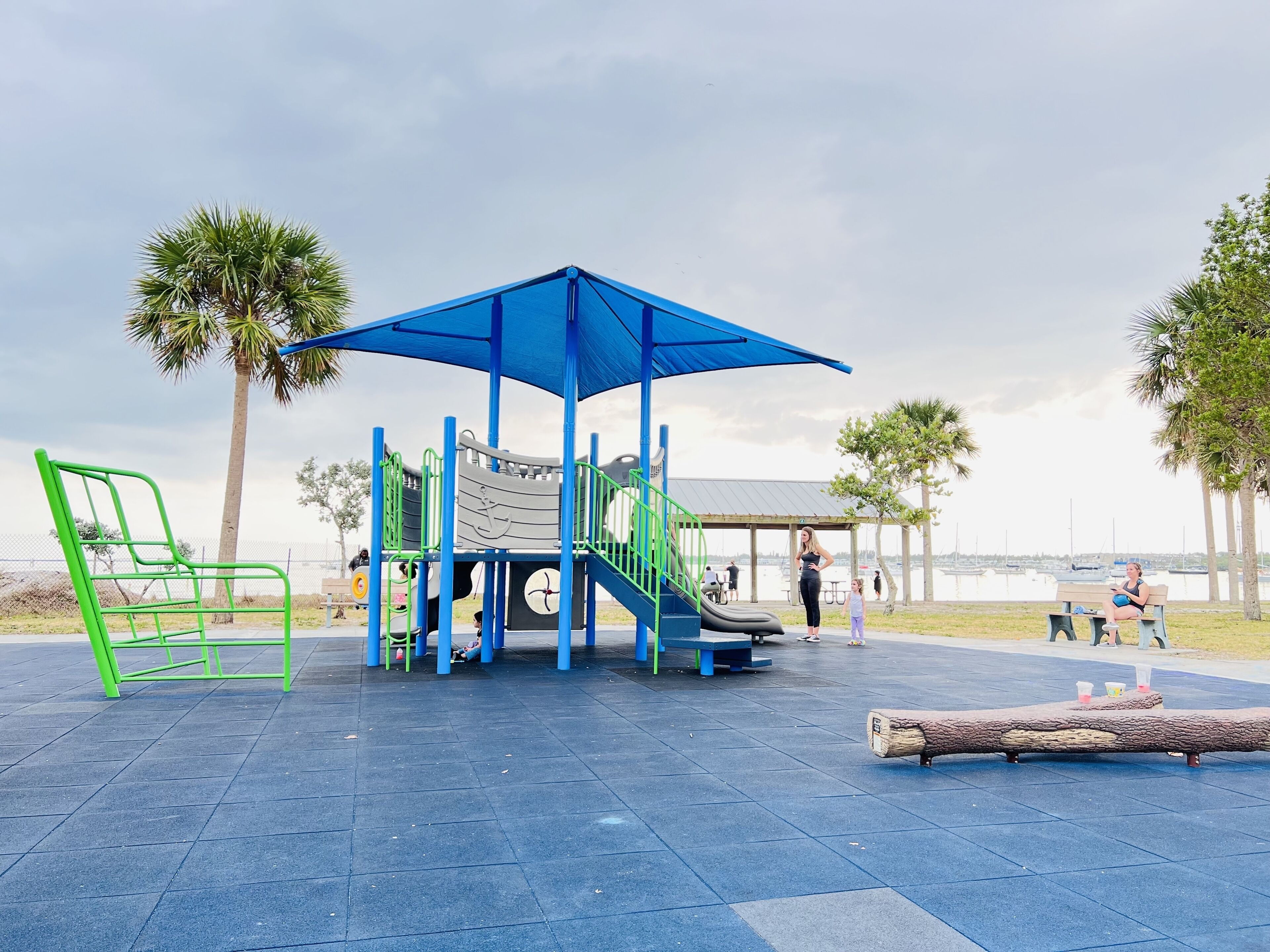 A playground with a blue canopy, green and blue play structures, and a bench.